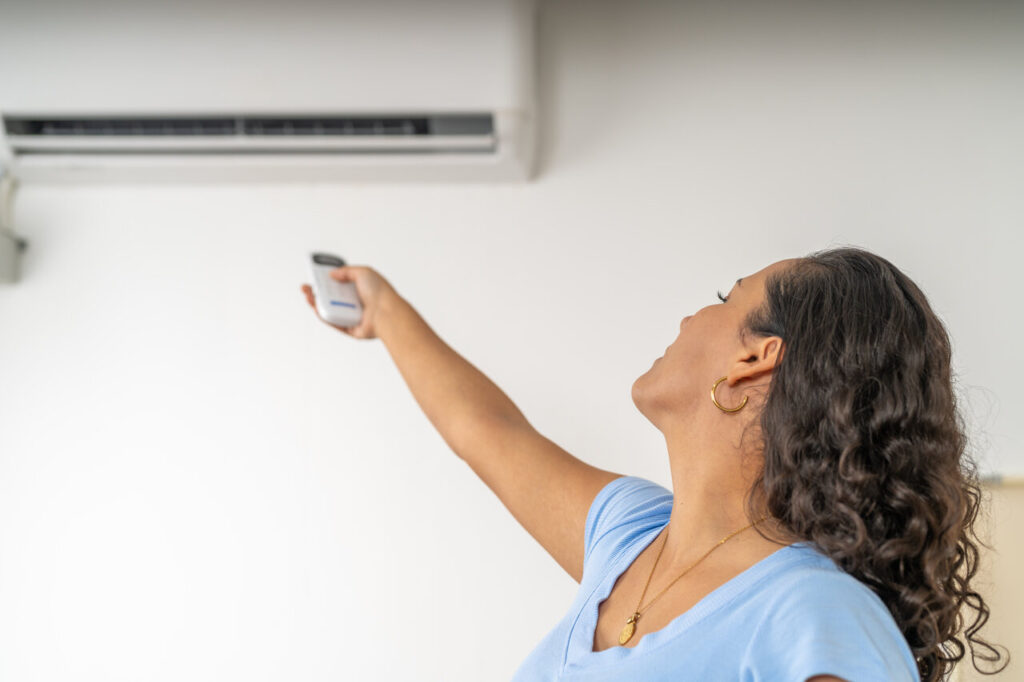 Woman Turning On Air Conditioning For Relief From Heat