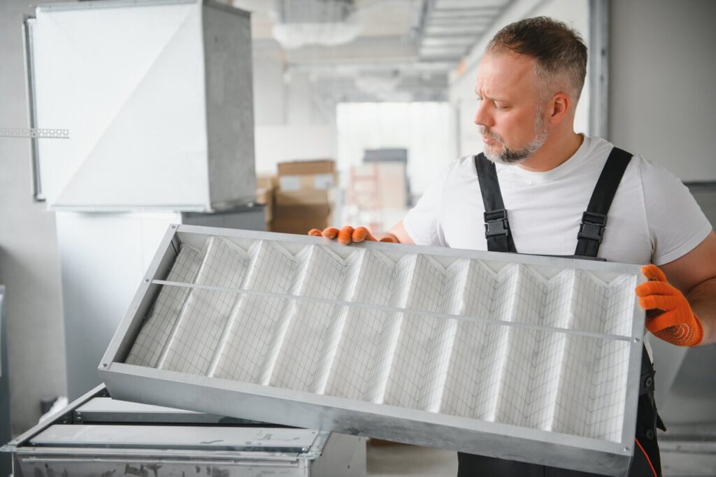 A Male Worker Holds An Air Filter For Air Conditioning In An Office Space Installation Of An Air Conditioner